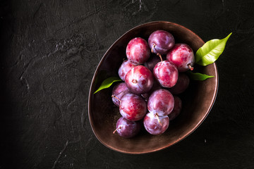 Whole fresh red violet blue plums and slices cut with knife in bowl on kitchen table