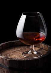 Glass of cognac brandy drink on top of wooden barrel.