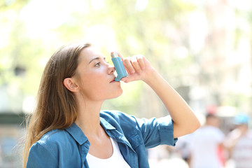 Asthmatic woman using a inhaler outdoors - obrazy, fototapety, plakaty