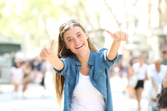 Joyful girl gesturing thumbs up in the street