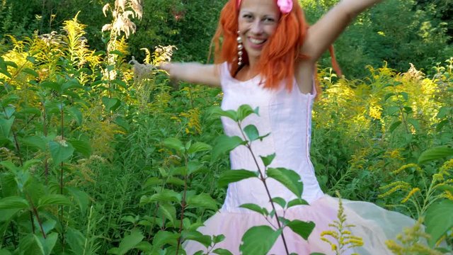 Smiling red hair woman has a fun at the sunny meadow at pink dress