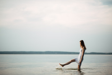 Fototapeta na wymiar Woman in summer dress standing on seashore and looking at horizon. Young beautiful girl standing in water