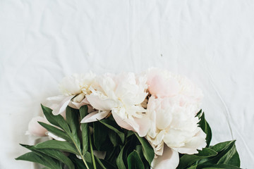 Obraz na płótnie Canvas Flat lay, top view of white peonies flower bouquet on white blanket background. Minimal summer floral concept.