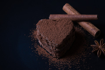 chocolate biscuit in the form of heart sprinkled with cocoa powder lies on a dark background next...