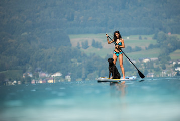 Beautiful woman standing on paddle board with her dog.