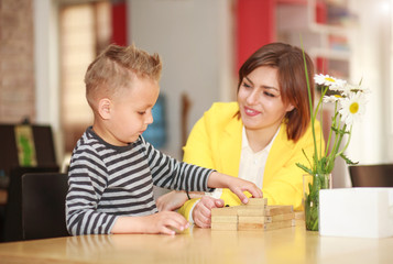 Young mother with baby son playing at home in room at table