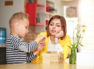 Young mother with baby son playing at home in room at table