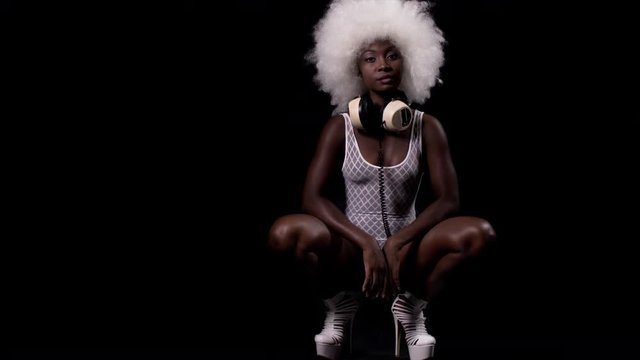 beautiful african female model in large afro wig posing crouched in white lingerie and headphones.