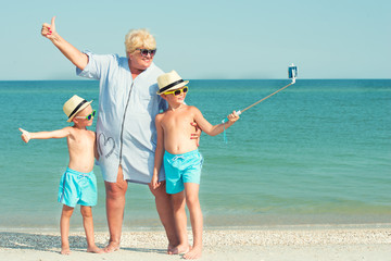 Grandmother with her grandchildren are resting on the sea, they are make a selfie on the beach.