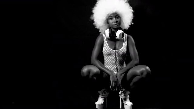 beautiful african female model in large afro wig posing crouched in white lingerie and headphones.