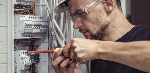 a male electrician works in a switchboard with an electrical connecting cable