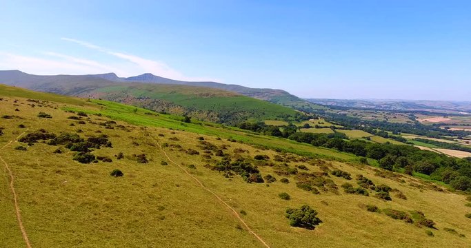 Flying over colourful valley of Brecon Becons in South Wales towards mountain range .