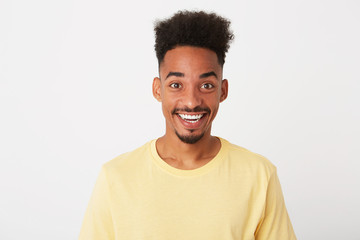 Portrait of cheerful amazed african american young man with curly hair wears yellow t shirt looks excited and smiling isolated over white background