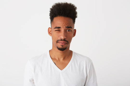 Closeup of playful handsome african american young man with curly hair wears t shirt looks serious and winking isolated over white background