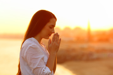 Profile of a concentrated woman praying at sunset - obrazy, fototapety, plakaty