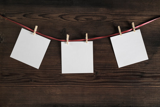 Blank photo paper attach to rope with clothespins on wooden background. Template for placing your design.