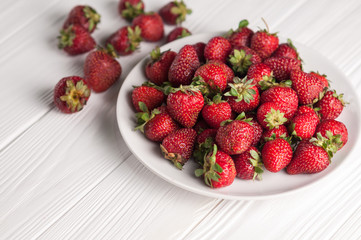 Fresh strawberries in a plate on a white wooden background.