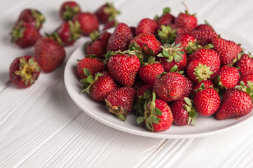 Fresh strawberries in a plate on a white wooden background.