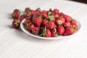 Fresh strawberries in a plate on a white wooden background.