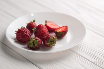 Fresh strawberries in a plate on a white wooden background.