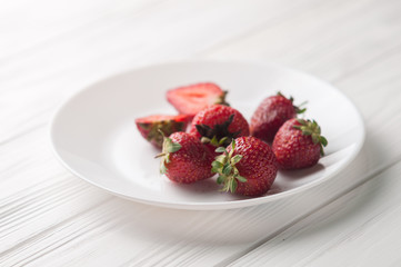 Fresh strawberries in a plate on a white wooden background.