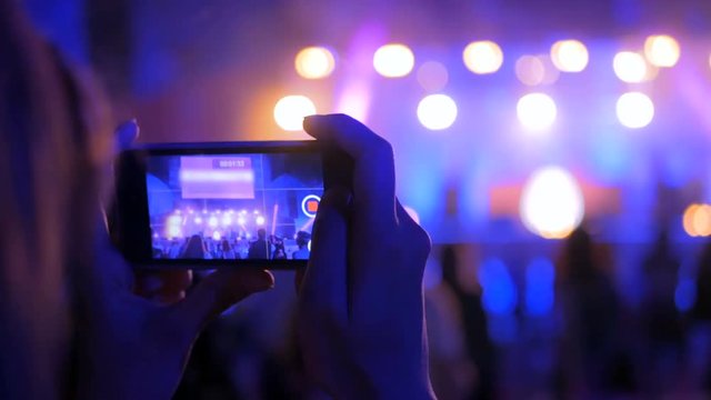Unrecognizable woman hands silhouette taking photo or recording video of live music concert with smartphone at night. Photography, entertainment and technology concept