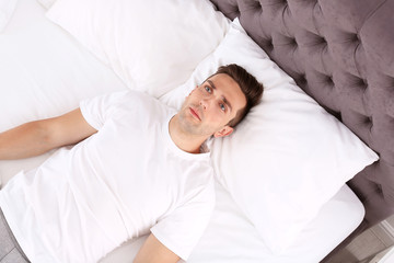 Young man lying in bed at home, top view. Sleep disorder