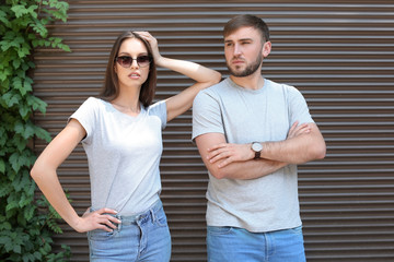 Young couple wearing gray t-shirts near wall on street.