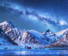 Milky Way above houses and snow covered mountains in winter at night. Starry sky, small village, snowy rocks in Lofoten Islands, Norway. Nordic landscape with milky way, water, ridge, buildings. Space - Powered by Adobe