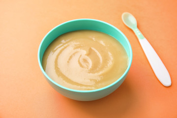 Bowl of healthy baby food on color background