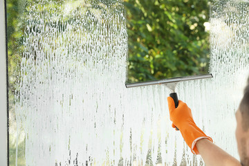 Male janitor cleaning window with squeegee, closeup