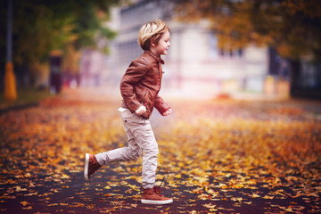 smiling young boy, kid having fun in autumn city park among fallen leaves