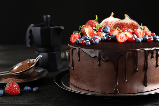 Fresh delicious homemade chocolate cake with berries on table against dark background