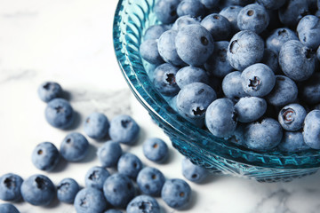 Bowl with fresh blueberries on marble table, closeup