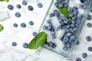 Flat lay composition with juicy blueberries, green leaves and ice on marble table