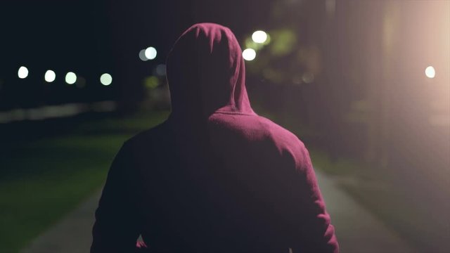 The male in a hood walking on the night street and smoking. slow motion