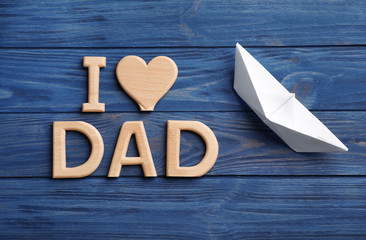 Flat lay composition with phrase I LOVE DAD and paper boat on wooden background. Father's day celebration