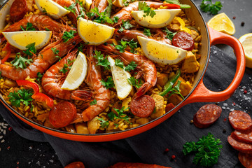 Traditional paella in the fry pan with chicken, prawns, spicy chorizo, lemon and glass of white wine.