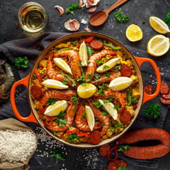 Traditional paella in the fry pan with chicken, prawns, spicy chorizo, lemon and glass of white wine.