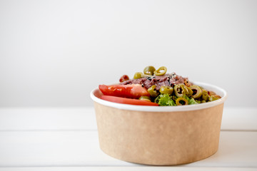 Take away salad in disposable craft paper bowl on white background. Minimalism food photography concept. Mockup, copyspace