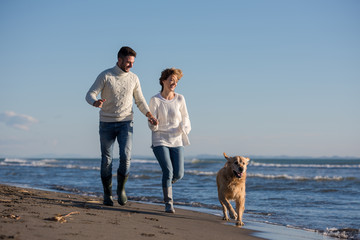 couple with dog having fun on beach on autmun day