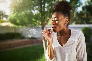 happy african american woman smoking marijuana joint in back yard