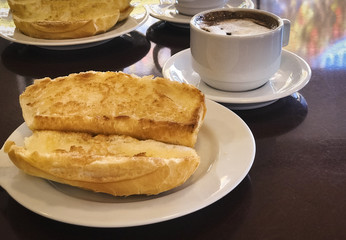 Breakfast at Brazil with french bread toasted with butter on the plate with capuccino on table.