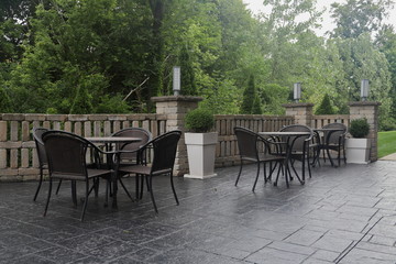 Tables and Chairs on hotel patio in the morning sunlight with greenery in the background