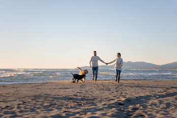 couple with dog having fun on beach on autmun day