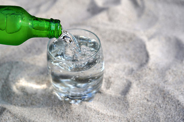 Pouring mineral water in the glass on beach sand.