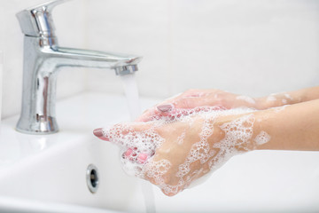 Washing hands with soap under the faucet with water.