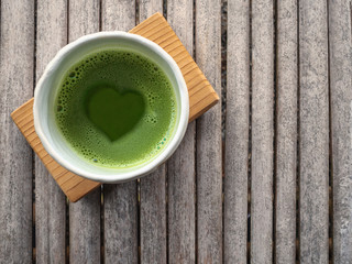Top view of organic green tea matcha with heart shape in foam  in white japanese style ceramic bowl after ceremony processing with copy space