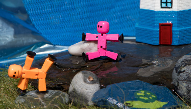 Stickbot toys posed on rocks near lighthouse in summer sunshine, whimsy, cute, macro.