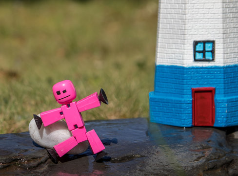 Stickbot toys posed on rocks near lighthouse in summer sunshine, whimsy, cute, macro.